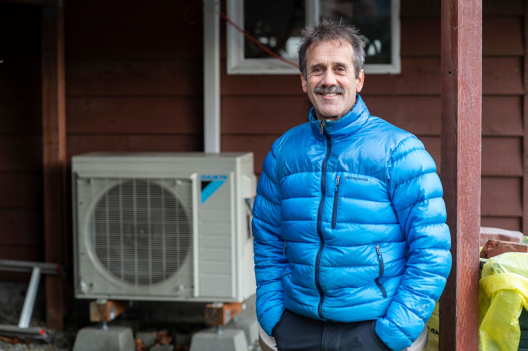 Andy Romanoff. Executive Director of Alaska Heat Smart, stands in front of a heat pump at his home in Juneau, Alaska, on Monday, Nov. 13, 2023. (Michael Penn for Earthjustice)