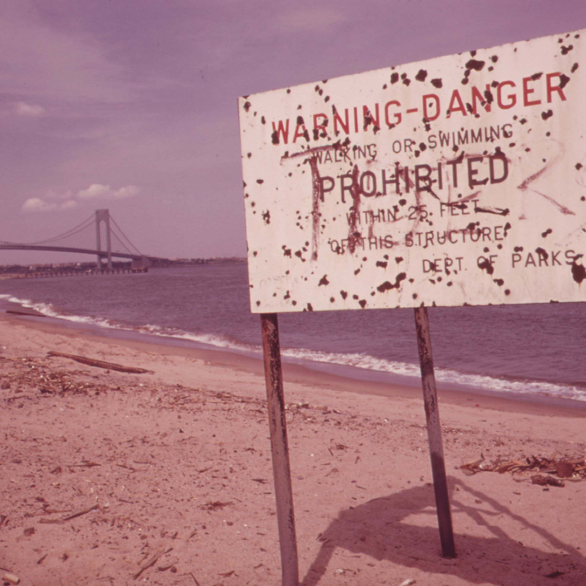 A warning sign of polluted water at Staten Island Beach with the Verrazano-Narrows Bridge in the background, in June 1973.